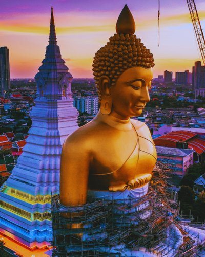 Giant golden Buddha statue beside a temple spire at sunset